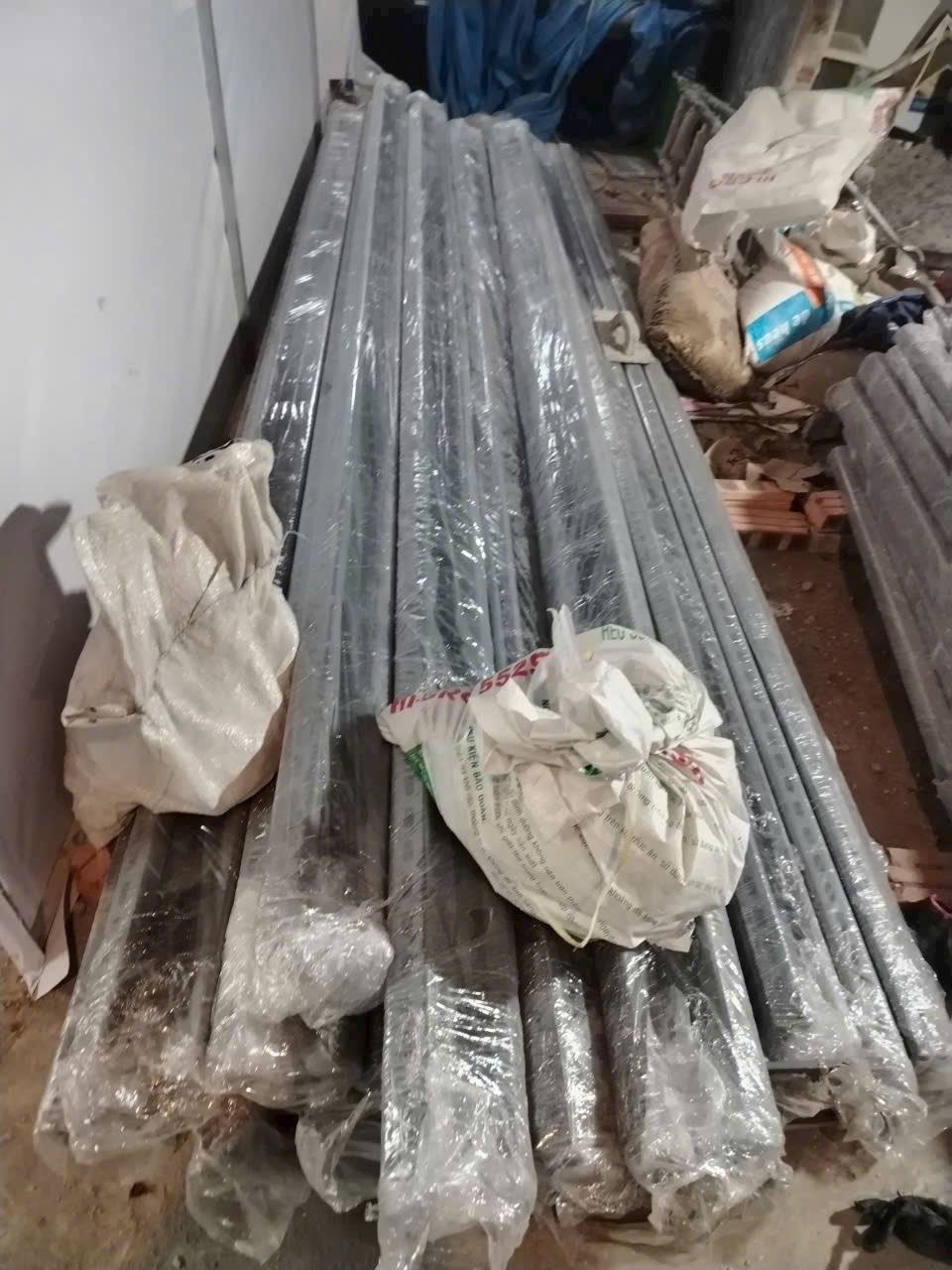 Bó ống thép dài được bọc nilon đặt trên nền kho cùng vài bao tải dựng bên cạnh